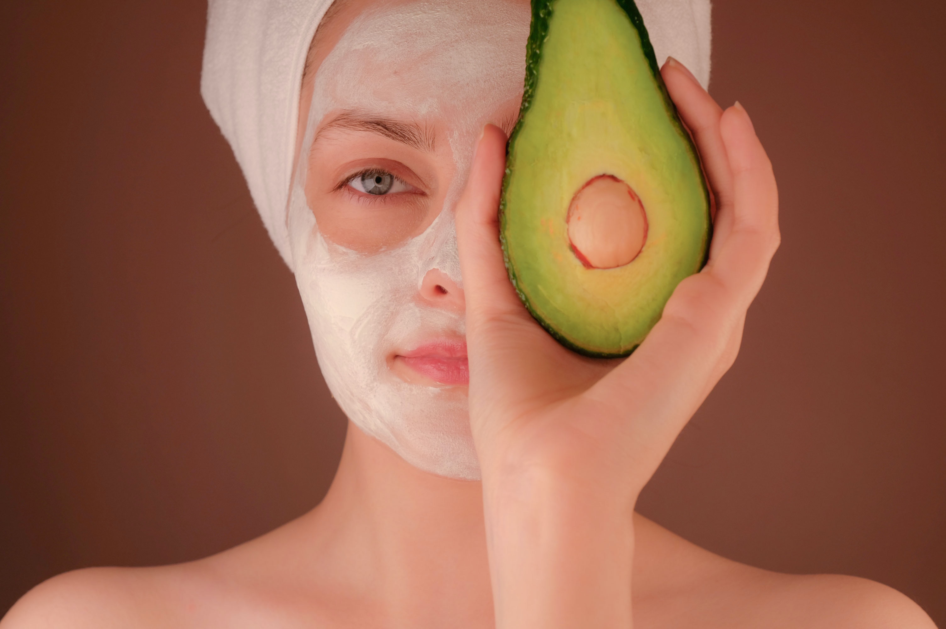 woman with a facial mask holding an avocado